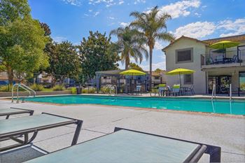 A pool area with a table and chairs and umbrellas.
